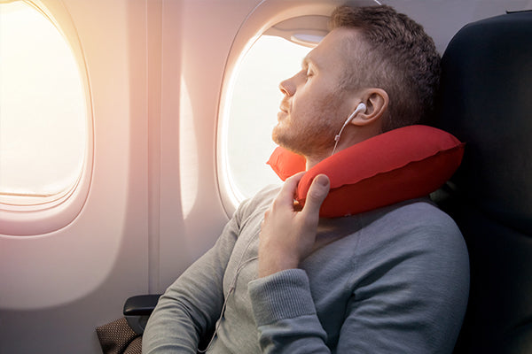 man on a plane with a neck pillow and earbuds