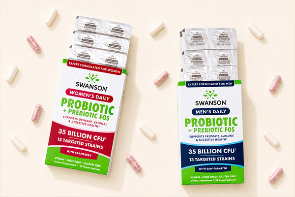 Two Swanson probiotic boxes, Women’s Daily and Men’s Daily, with scattered pink and white capsules