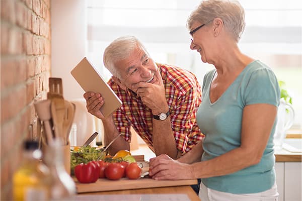 Senior man and woman in the kitchen chopping vegetables