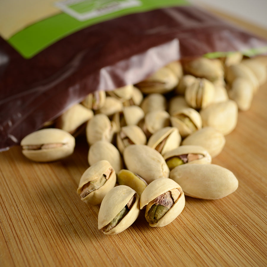 NWF1143 | close-up of pistachios spilled from a partially visible bag on a wooden board showing shells and green kernels