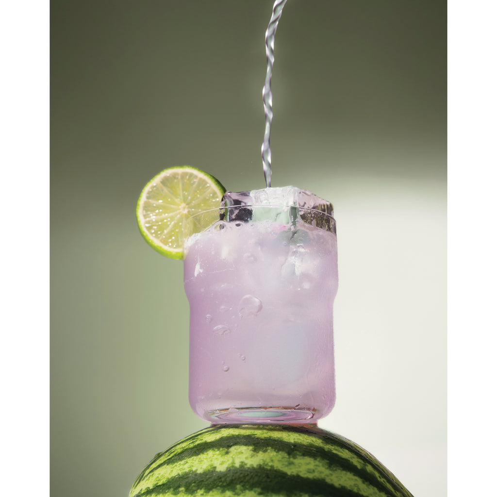 KTO004 | Water pours into a pink cocktail in a glass garnished with a lime slice, set on a watermelon - Thumbnail