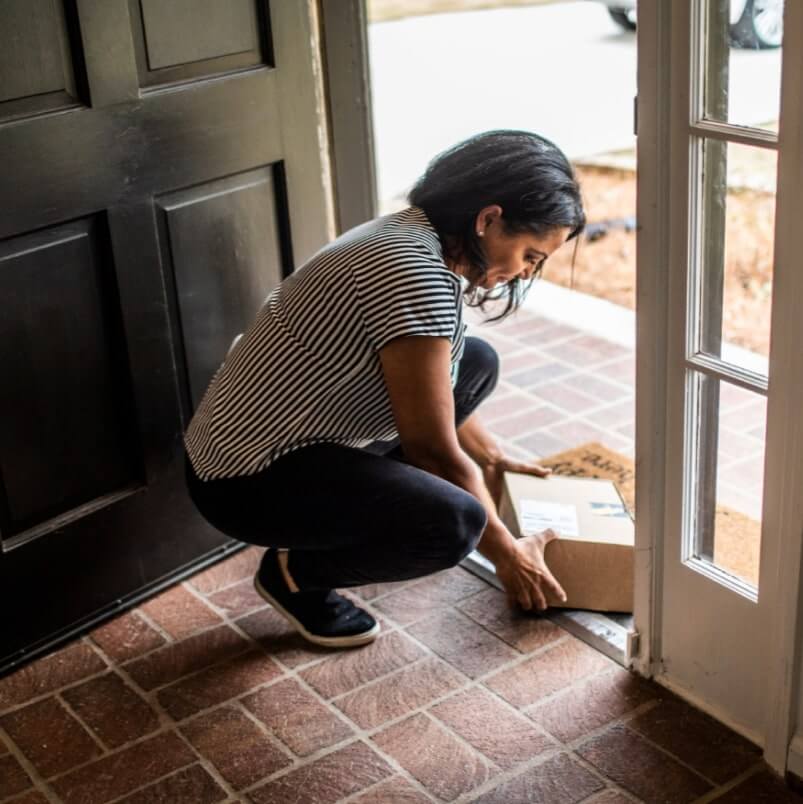 Woman opening a door with a package on a brick patio