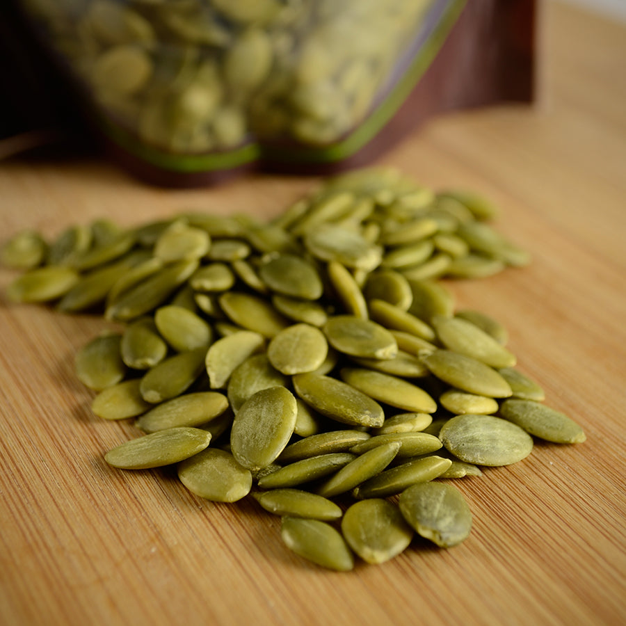 NWF1110 | pile of pumpkin seeds (pepitas) on wooden cutting board with resealable bag in background - Thumbnail